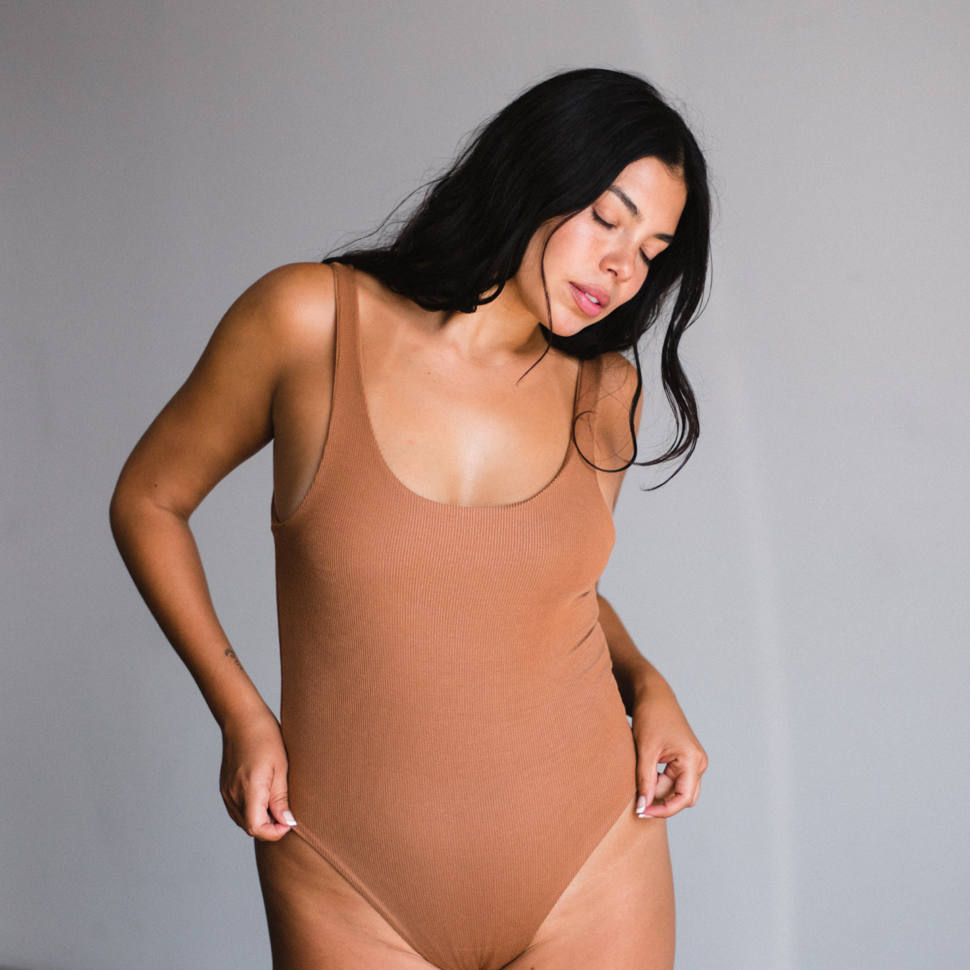 Model wearing maya nude, a caramel tone, bodysuit that is scoop neck style