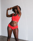 model with hand covering eyes laughing wearing red poppy square neck bralette and mid rise briefs in matching color